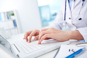 A medical professional is typing on a keyboard of an open laptop