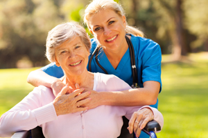 Female Nurse standing behind an elderly smiling patient in a wheelchair outside